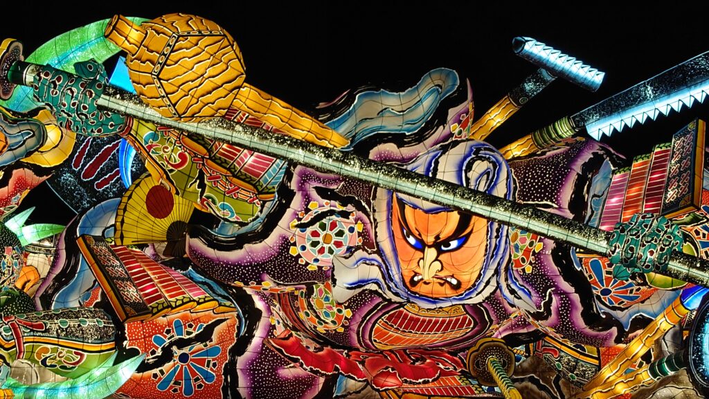 alt="A giant illuminated float parading through the streets during Aomori Nebuta Festival in Japan"